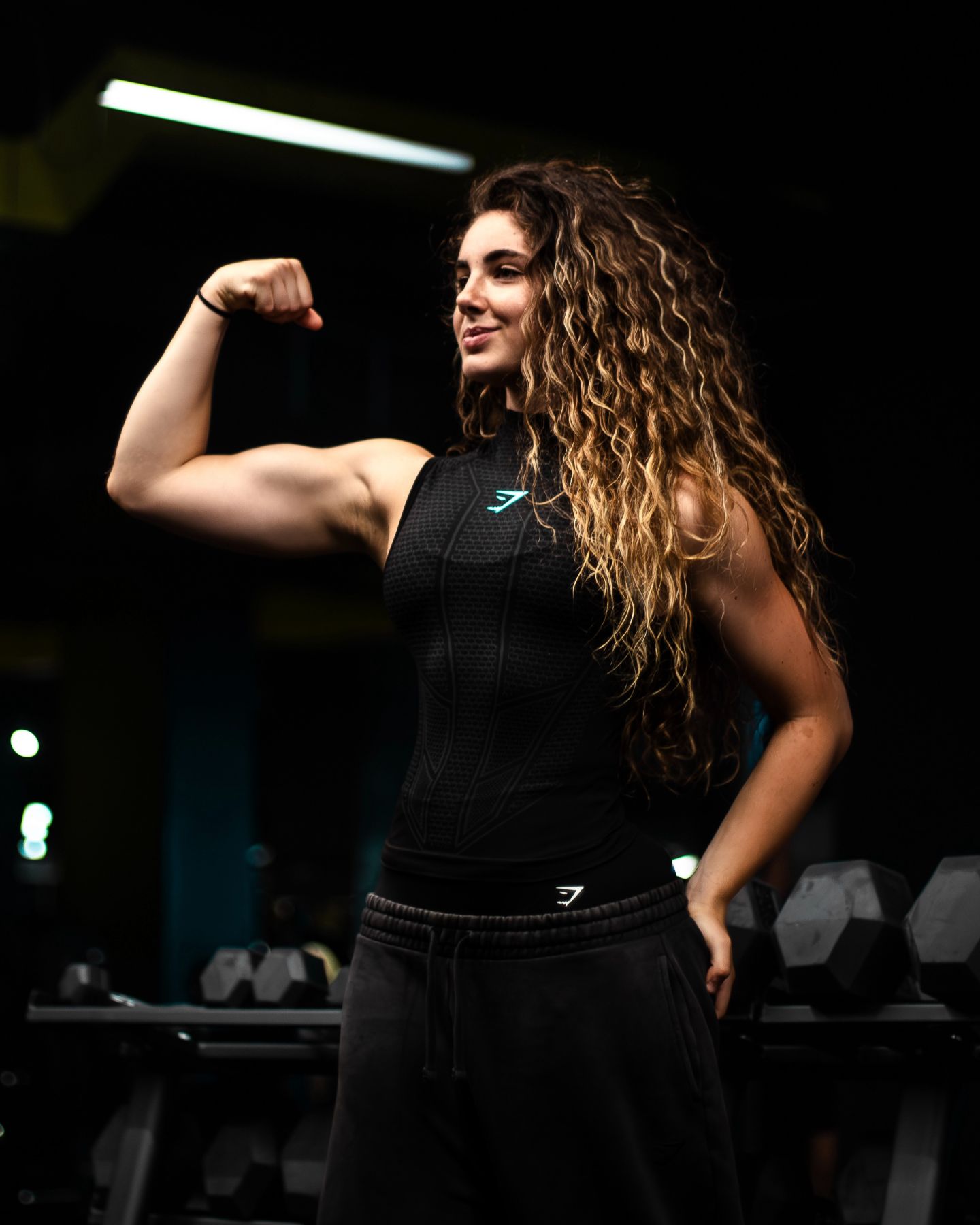 La coach flexiona el bíceps en el gimnasio.